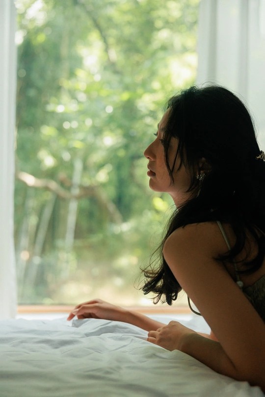 一个坐在白色床上的女人正在看窗户外面的景色