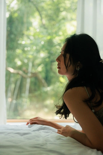 一个坐在白色床上的女人正在看窗户外面的景色