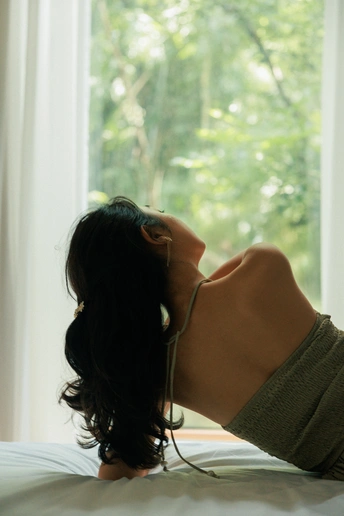 一位女性躺在床上 戴着耳机 凝视着窗外。