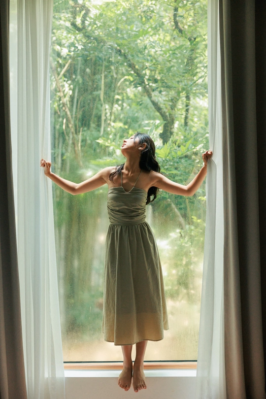 一位年轻女子站在打开的窗户前 窗帘也打开着。