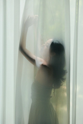 一位穿着白色连衣裙的女人站在窗户前