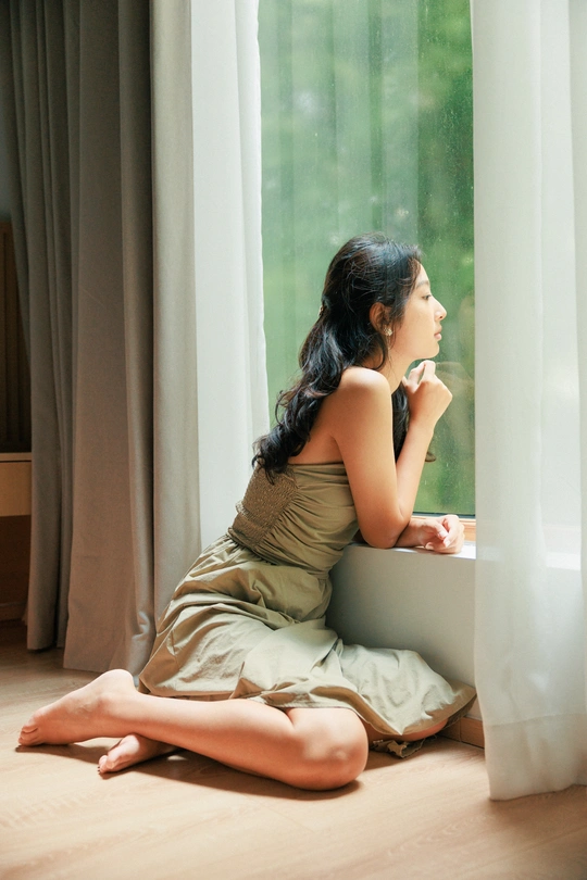 一个年轻女子坐在地板上 透过窗帘向外看。