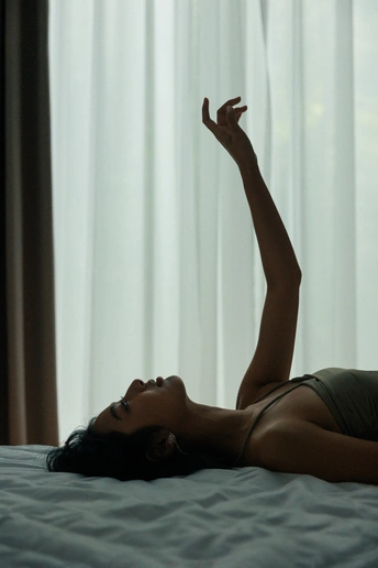 一个年轻女子躺在床上 她的手臂伸展在窗户前。