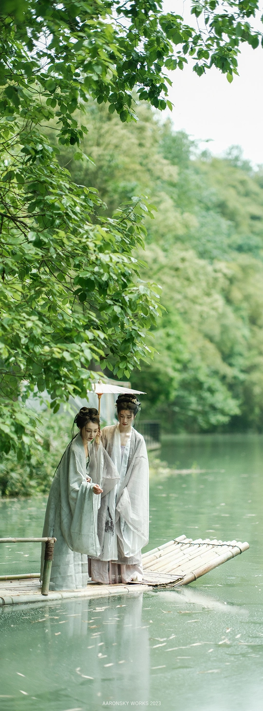 一位穿着长袍的男女站在一艘小船上 船上有一把雨伞 在河上。