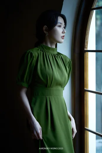 一位穿着绿色连衣裙的女人站在窗户前