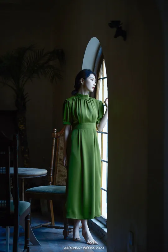 一个穿着绿色连衣裙和帽子站在有窗户的房间里的女孩