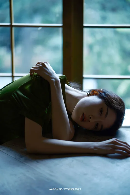 一位穿着绿色衬衫的年轻女子躺在地板上 面前是一扇窗户。