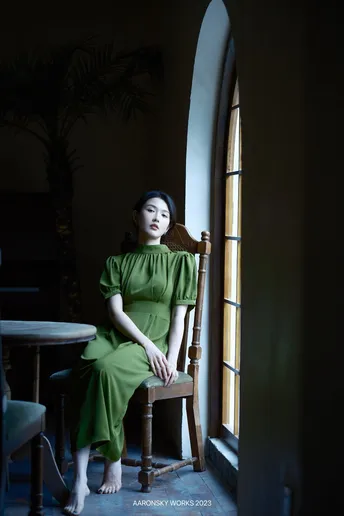 一个穿着绿色连衣裙的女人坐在一个带有窗户的房间里的一把椅子上