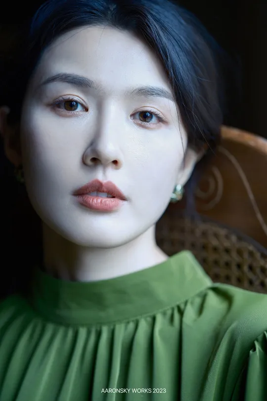 一位穿着绿色连衣裙的年轻女子在昏暗的光线下的人物肖像