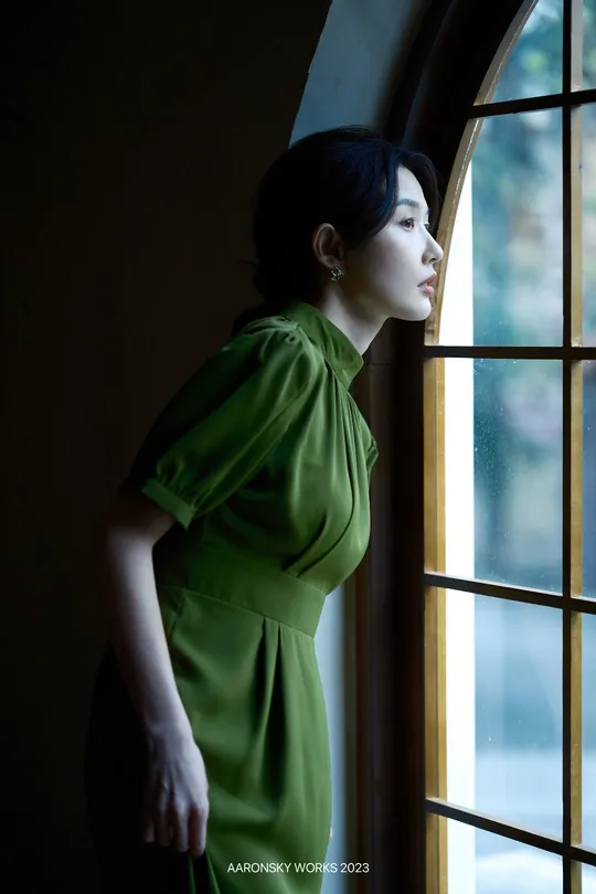 一位穿着绿色连衣裙的女人正在窗户旁向外看