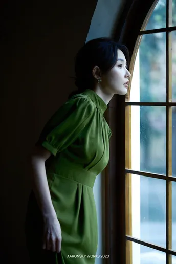 一位穿着绿色连衣裙的女人正在窗户旁向外看