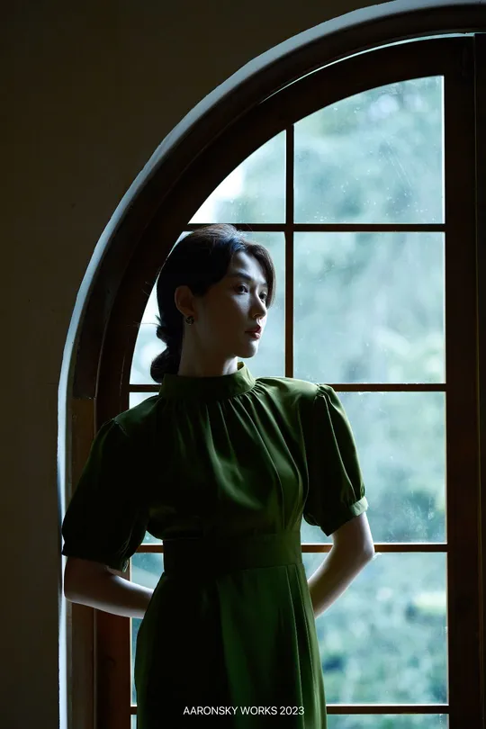 一位穿着绿色连衣裙的女人正在窗户旁向外看