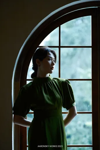 一位穿着绿色连衣裙的女人正在窗户旁向外看