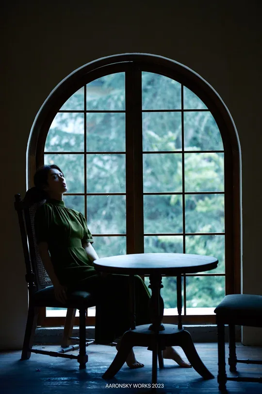 一个坐在黑暗房间里的桌子旁 凝视着窗外的大型窗户的男人