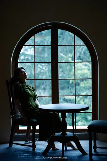 一个坐在黑暗房间里的桌子旁 凝视着窗外的大型窗户的男人