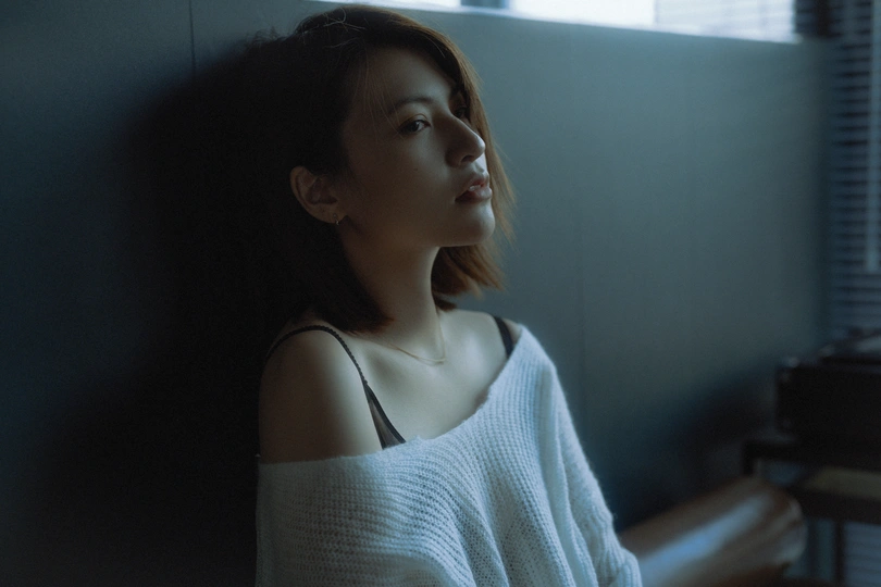 一个年轻女子坐在黑暗的房间里 窗外有一架白色的钢琴。