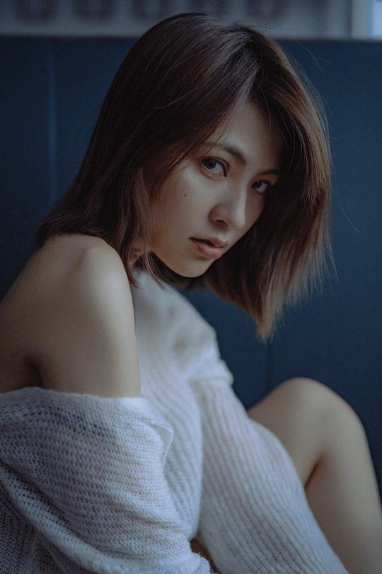 一位年轻女性坐在深蓝色房间里的蓝色沙发上 头发是白色的。