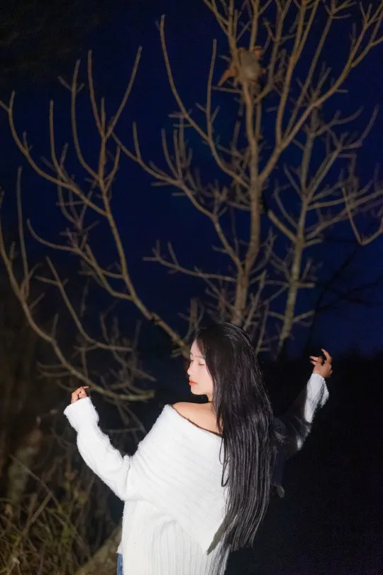 一位穿着白色毛衣站在夜晚外面的女人