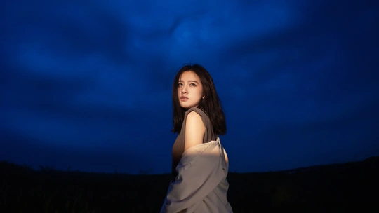 一位穿着白色连衣裙的年轻女子站在一个蓝色的夜晚田野中