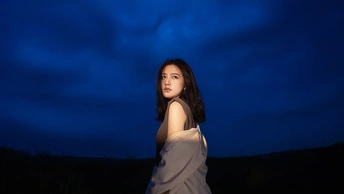 一位穿着白色连衣裙的年轻女子站在一个蓝色的夜晚田野中