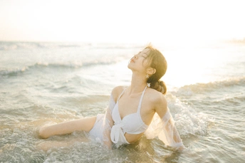 一位美丽的年轻女子穿着白色比基尼躺在海滩上的水中。