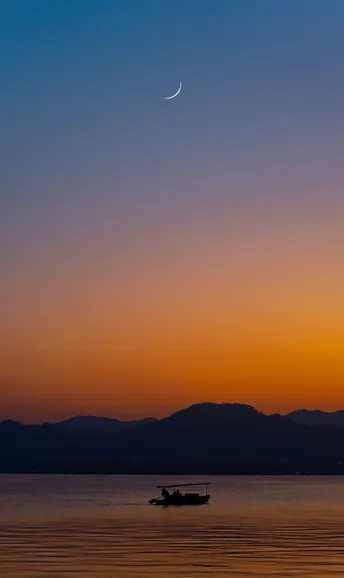 夕阳西下 远处有山 前景有小船。