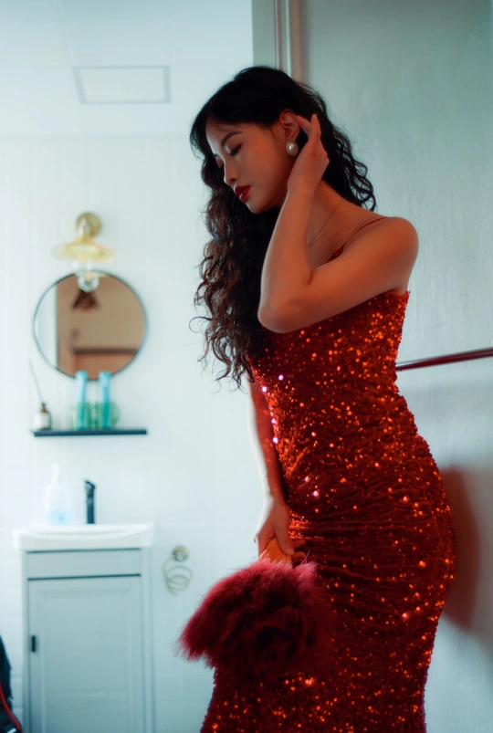 一位穿着红裙子的年轻女子站在一个房间的镜子前