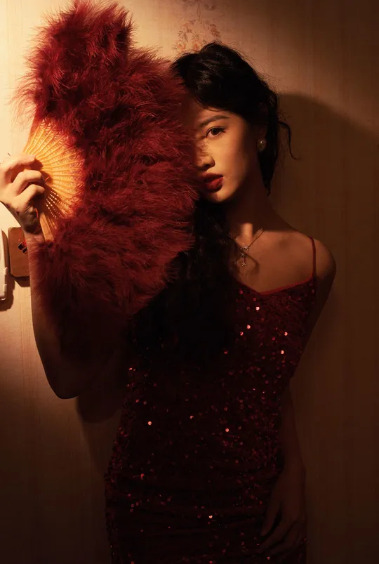 一位红发年轻女子站在一面墙前持扇姿势