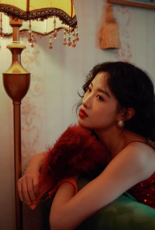 一个穿着红裙子的年轻女子坐在一个绿椅子上 在一个光线昏暗的房间里。