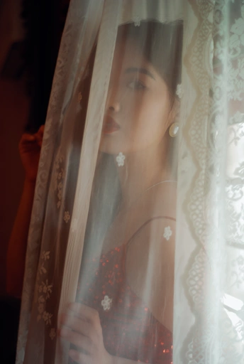 一位穿着红裙和面纱的年轻女子站在窗户前