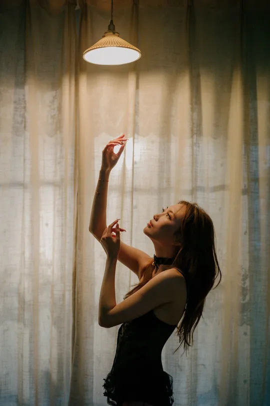 一个年轻女子站在一扇窗帘前 房间由手电筒照亮。