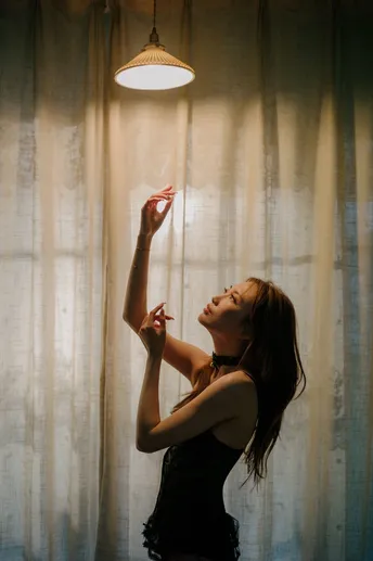 一个年轻女子站在一扇窗帘前 房间由手电筒照亮。