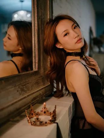 一个穿着黑色连衣裙的年轻女子站在浴室里 看着镜子里的自己的倒影。