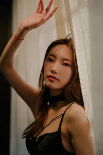 一位穿着黑色衣服的年轻女子在窗前摆姿势 窗帘在背后