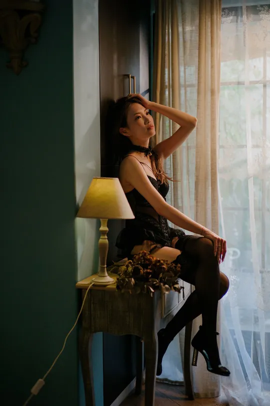 一个穿着连衣裙的年轻女子坐在一个带有窗户的房间里的一把椅子上