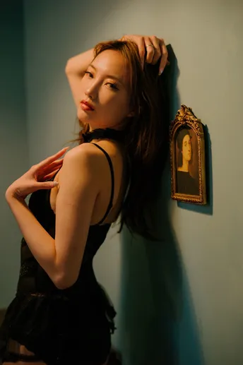 一位穿着黑色连衣裙的年轻女子靠在一间有镜子的房间里 