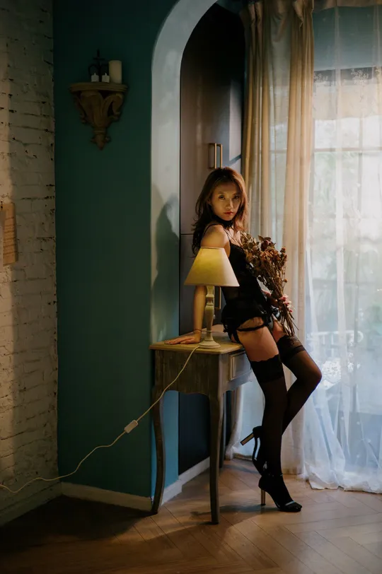 一个穿着黑色连衣裙和高筒靴子的年轻女子坐在桌子旁的一个房间里。