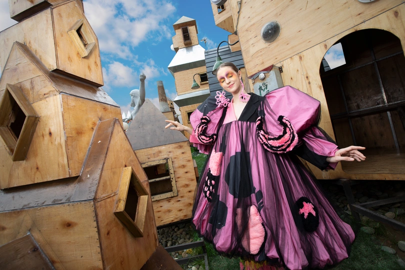一位穿粉色裙子的女人站在一栋木质建筑前 背景中有一座教堂。