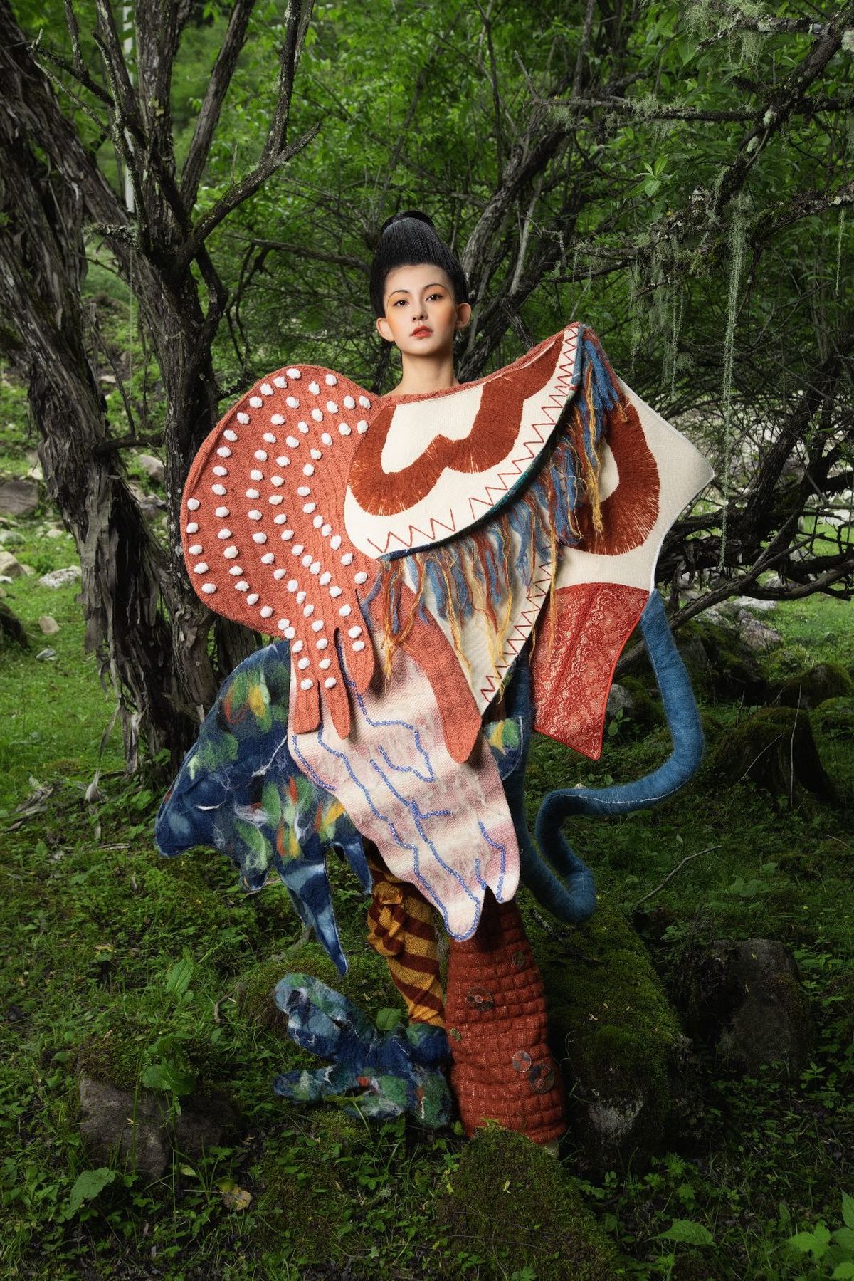 一位穿着艺术服装的女性在森林中与树木和一座雕像合影。