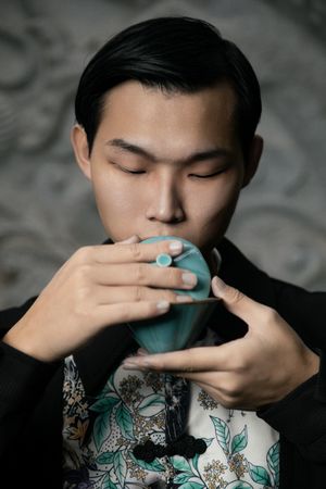 一个年轻人手里拿着一只蓝色的杯子 正在喝茶或咖啡 将杯子递到嘴边。