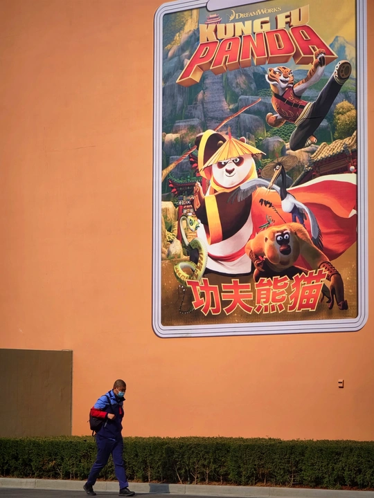 一个人走过一条街道 街边有一栋建筑上挂着一张电影海报。