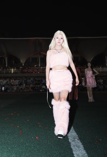 一位模特在时装秀上穿着粉色高筒靴走下 runway。