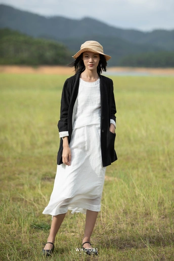 一个戴黑色帽子穿着白色裙子的年轻女子在田野中行走