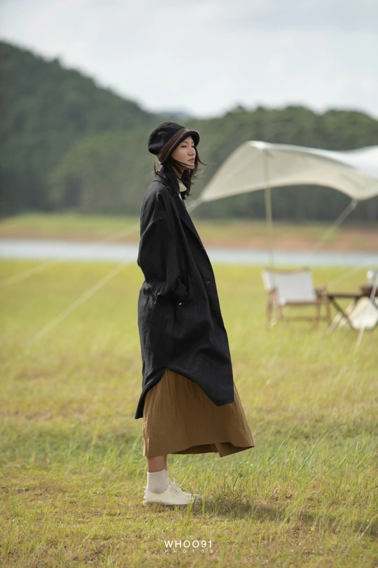 一位穿着黑色外套和裙子的女人站在一个田野里 手里拿着一把雨伞。