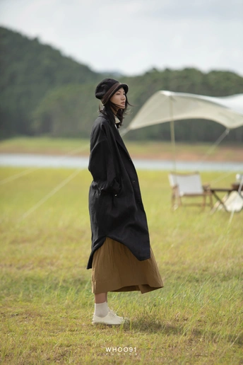 一位穿着黑色外套和裙子的女人站在一个田野里 手里拿着一把雨伞。