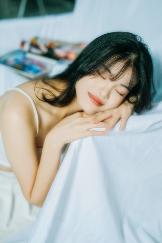 一个漂亮的年轻女人躺在床上 用手盖着一条白色毯子