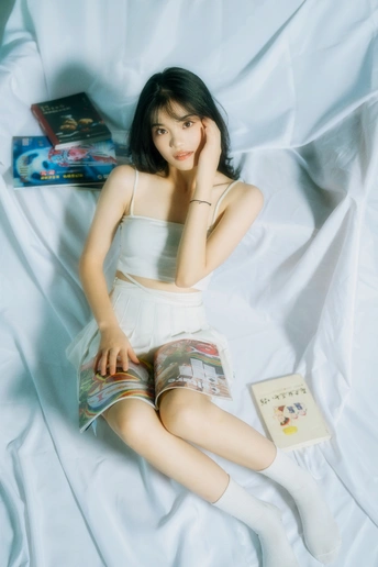 一个躺在床上的年轻女人 床上有白色床单和一本书