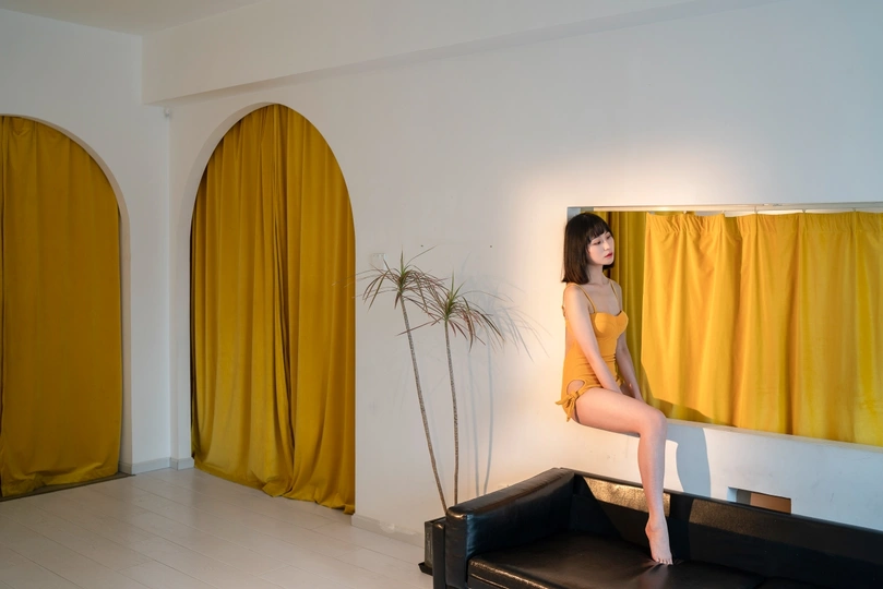 一个穿着黄色连衣裙的年轻女子盘腿坐在一个挂着黄色窗帘的房间里的黄色支架上