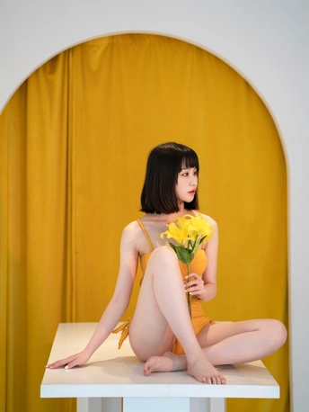 坐在白色桌子上的一位身穿黄色连衣裙、手捧鲜花的年轻女子