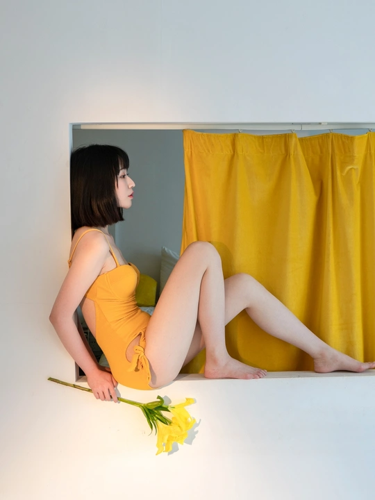 一个穿着橙色连衣裙的年轻女子盘腿坐着 手里拿着一朵黄色的花
